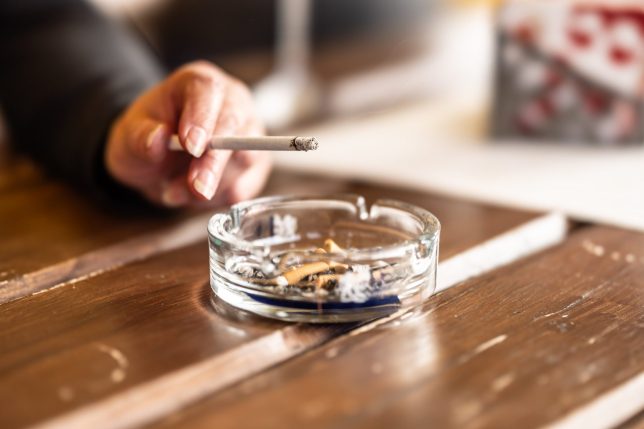 Smoker's hand holding a burning cigarette and flicking the ash into an ashtray