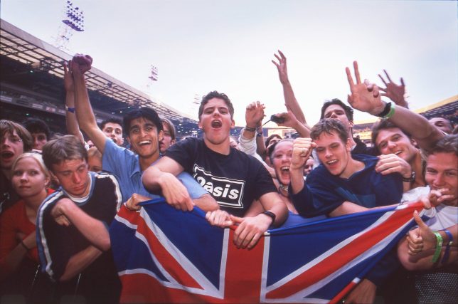 Oasis fans holding a union jack flag in the audience at Wembley Stadium, London, 21st July 2000. (Photo by Patrick Ford/Redferns)