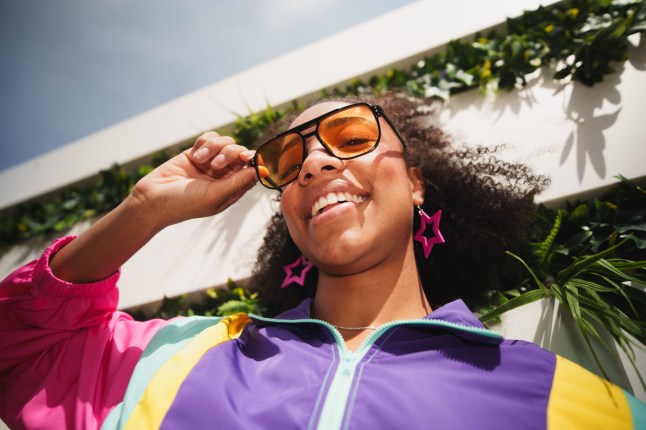 Young woman smiling, wearing colorful jacket and orange sunglasses outdoors