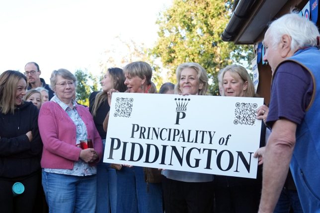 Local residents pose with a ?Principality of Piddington? sign in the village of Piddington, Oxfordshire, after they voted overwhelmingly to become an independent state in a symbolic ?referendum?. The village of around 350 residents held the vote after the Government said it wanted to set up a migrant camp close by. Picture date: Wednesday September 16, 2026. PA Photo. Photo credit should read: Joe Giddens/PA Wire