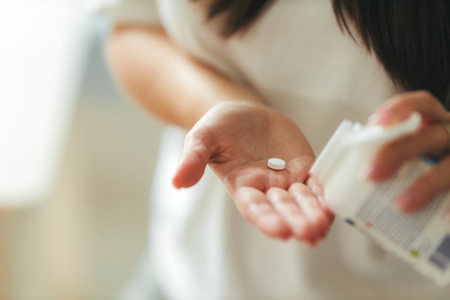 Close-up of young adult woman at home during daytime pouring a vitamin tablet from a supplement bottle into her hand.