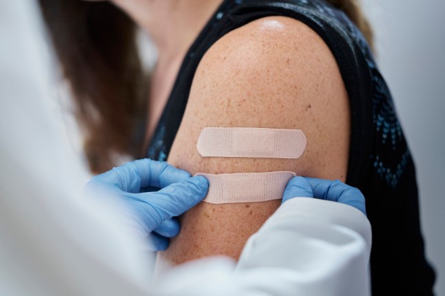 Rear view of a female young doctor with gloves giving second adhesive bandage to a caucasian young woman after the dose of the vaccine against a blurred background