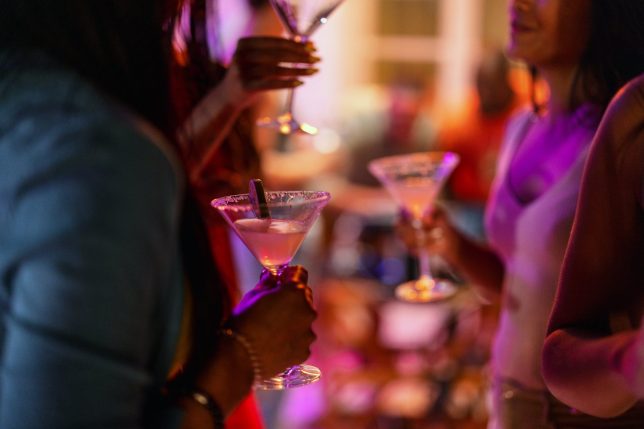 Close-up of a martini glass held by a female at a bar with purple lighting. Delicious summer cocktail.