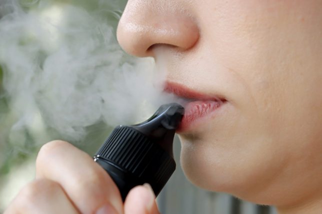 Closeup of woman smoking electronic cigarette and enjoying smoke. Girl smokes and exhaling flavored steam. Concept safe way of smoking, how to stop smoking