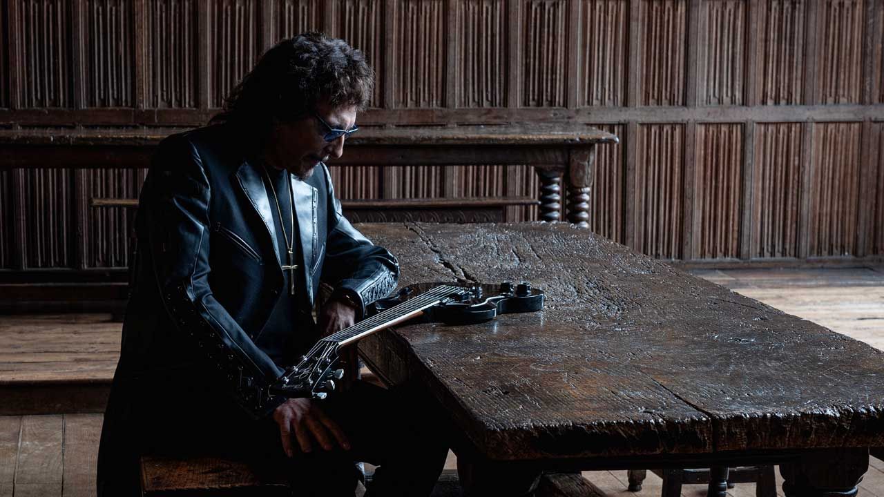 Tony Iommi sitting at a wooden table with a Gibson SG
