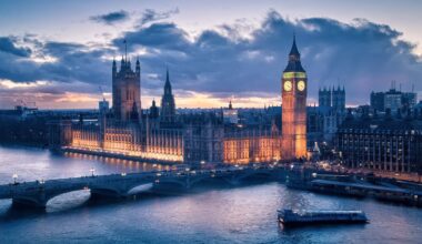 A view of the Houses of Parliament and Big Ben in London, illuminated at sunset with the River Thames in the foreground.