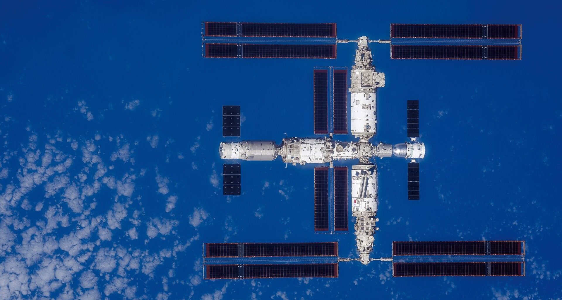 a large T-shaped space station is seen from above with Earth below it
