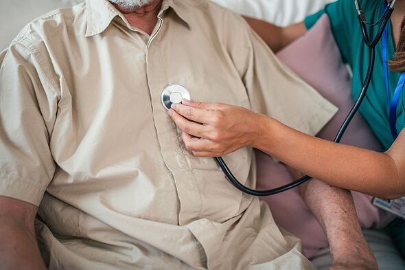 A senior man breathes deeply as a nurse examines his lungs using a stethoscope during a home visit