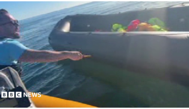 Anti-migrant campaigner leaning out of a boat appearing to hold a knife and to be shouting