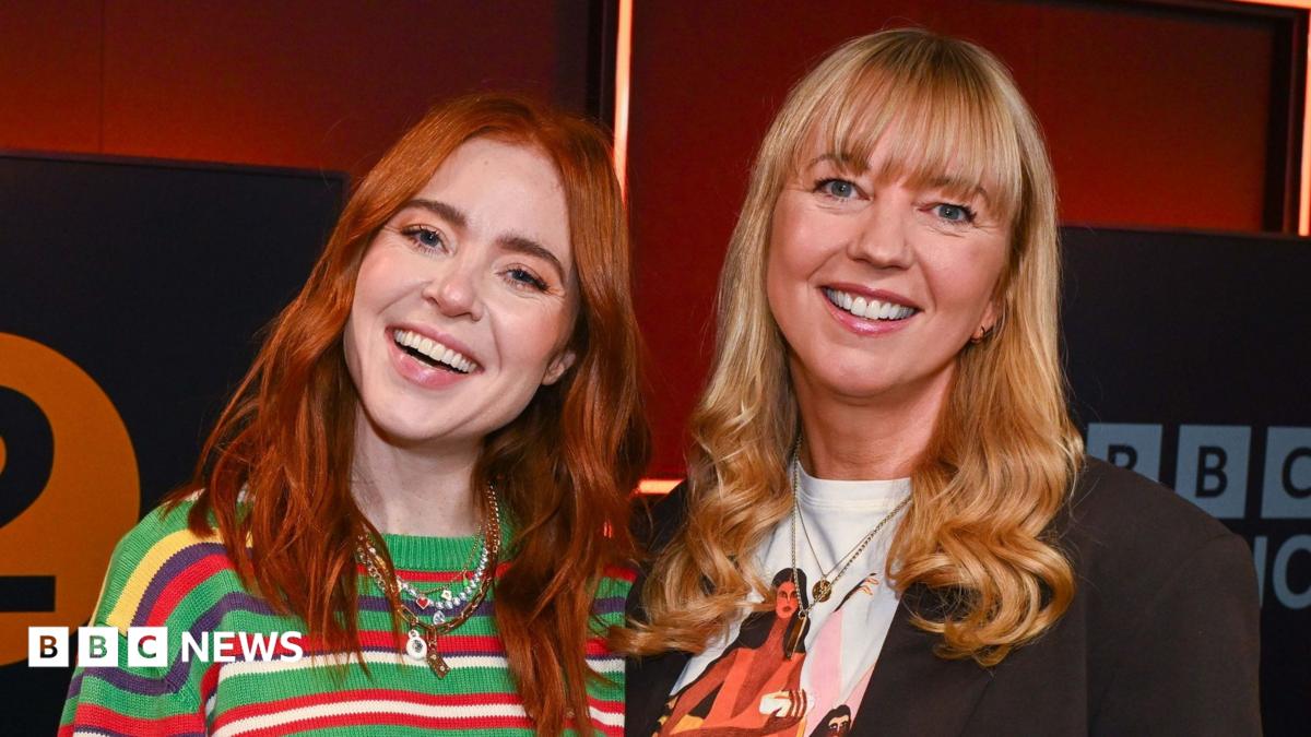 Angela Scanlon and Sara Cox standing and smiling together in front of the BBC Radio 2 logo