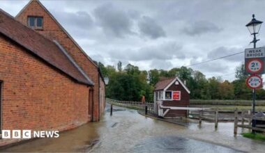 Totton Tide Mill area flooded after a burst water main.  Brick building to the left , wooden hut for toll bridge and wooden fence to the left.