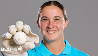 A smiling Alice Capsey holds up a ball while wearing wicketkeeper gloves
