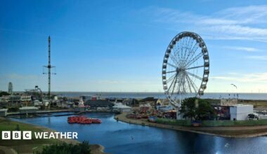 A seaside scene in Skegness with a big wheel and a funfair, the skies are blue