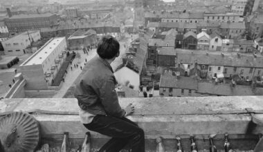a historical black-and-white photo of a boy seated on a parapet, with rows of glass bottles filled with rags like napalm, looking down on a town