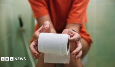 A teenage girl sits on the toilet, holding toilet paper in her hands