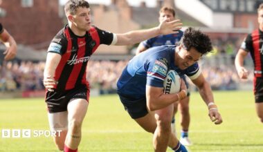 Wakefield Trinity's Isaiah Vagana, in blue, ducks under the arm of Warrington Wolves' Josh Thewlis, in red and black stripes, as he scores a try.