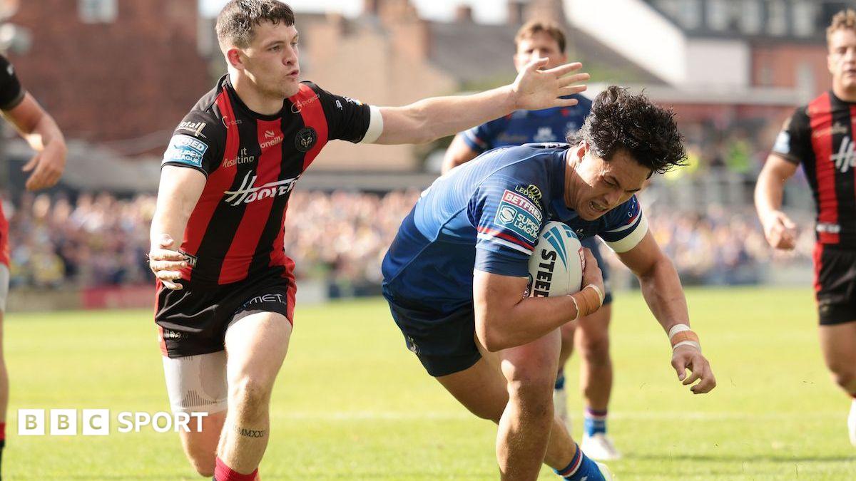 Wakefield Trinity's Isaiah Vagana, in blue, ducks under the arm of Warrington Wolves' Josh Thewlis, in red and black stripes, as he scores a try.