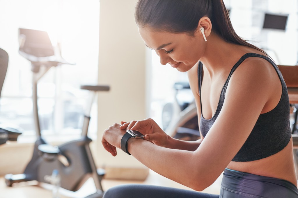 A woman in sports bra and leggings checking her smart watch at the gym.
