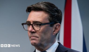 Britain's Prime Minister Andy Burnham attends a meeting with Canada's Prime Minister Mark Carney, he wears a black suit and white shirt. A Union flag hangs in the background.