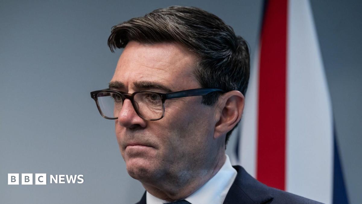 Britain's Prime Minister Andy Burnham attends a meeting with Canada's Prime Minister Mark Carney, he wears a black suit and white shirt. A Union flag hangs in the background.