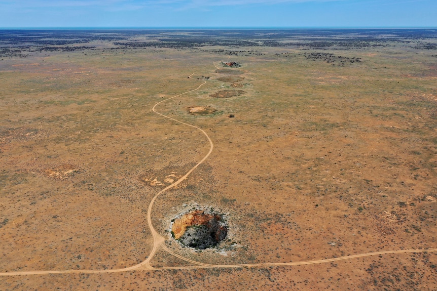 A drone shot of a vast, flat landscape, with a few large circular rock openings on the ground