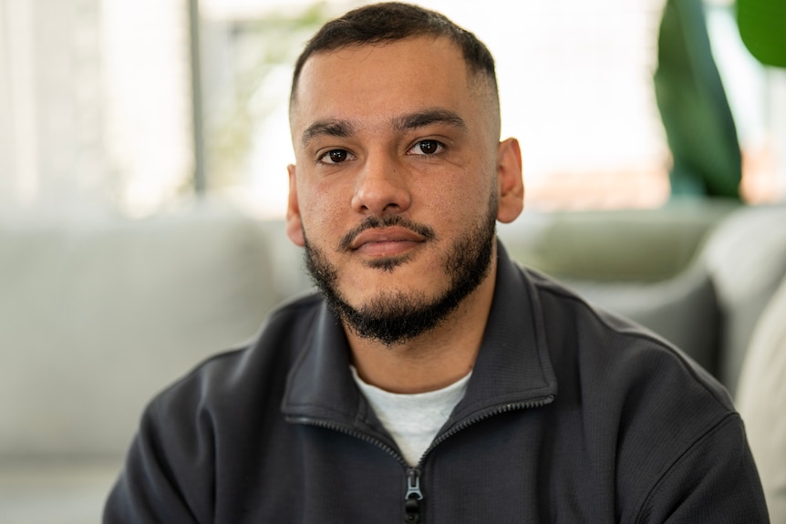 Man with dark black hair looking at camera, wearing hoodie