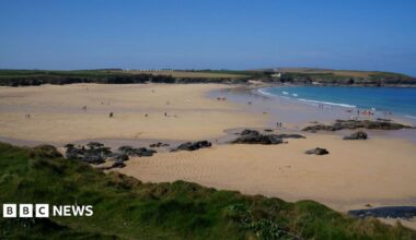 The image shows a wide sandy beach. There is a number of rocks within the sand and cliff faces surrounding the beach.