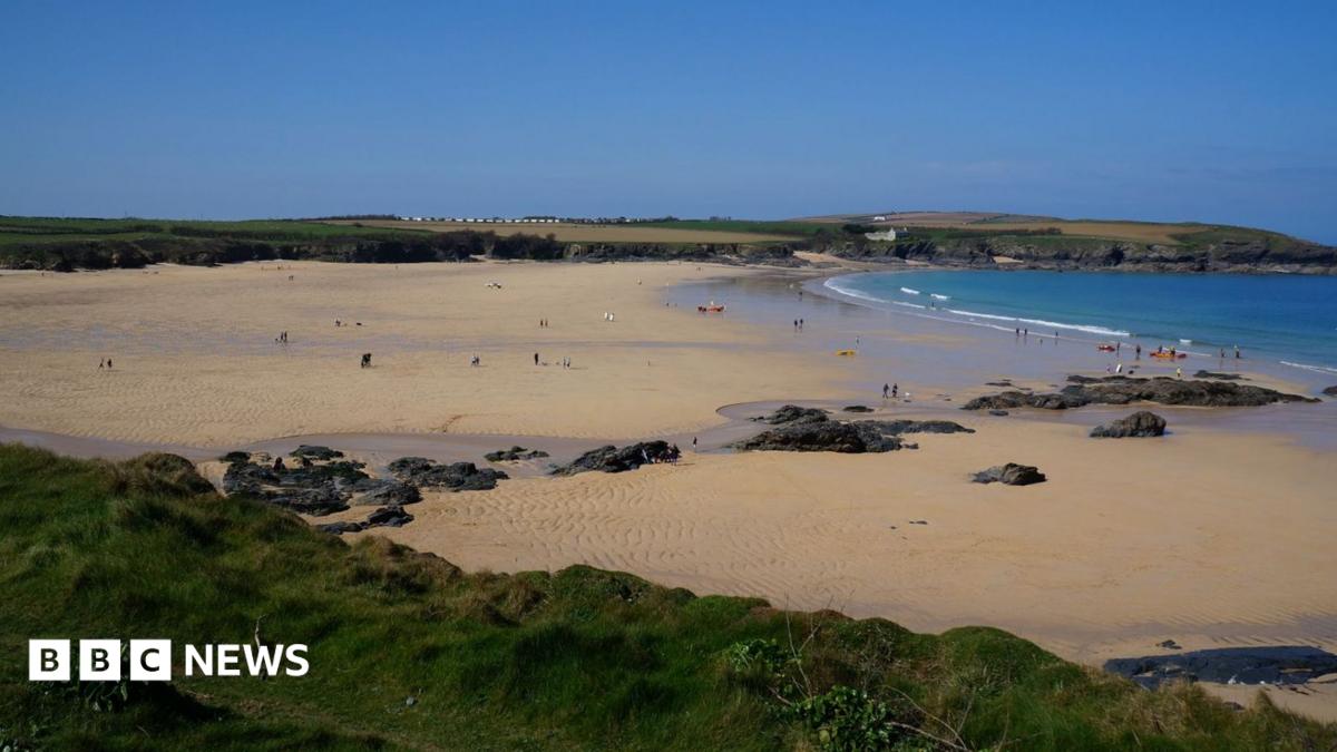 The image shows a wide sandy beach. There is a number of rocks within the sand and cliff faces surrounding the beach.