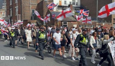 Anti-migration protesters waving St George flags and flanked by police officers