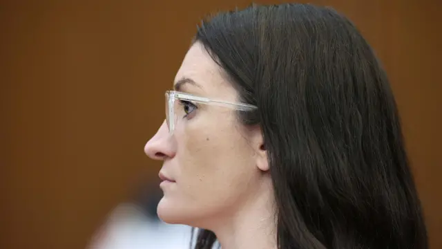 A close up shot of the side of a woman's head, she stares ahead and has long brown hair and wears glasses