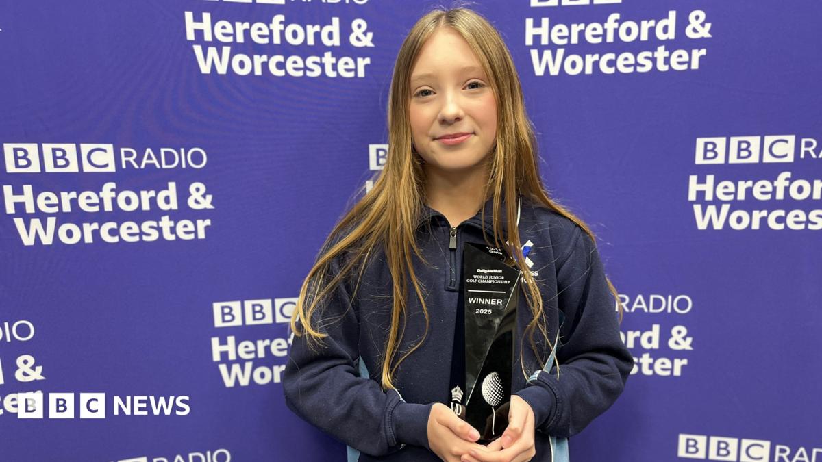 A 13-year-old girl with long dark blonde hair, wearing a dark blue quarter-zip jumper and holding a black trophy reading "winner 2025". She is standing in front of a purple backdrop reading "BBC Radio Hereford & Worcester"