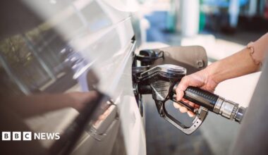 A hand gripping a fuel pump inserted into a white car.