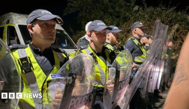 A row of police officers in high vis and holding shields stood facing crowds.