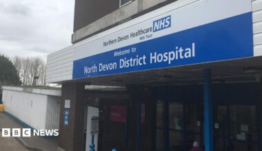Outside one of the entrances to the North Devon District Hospital site. A blue and white sign with the hospital's name on it are above the main doors.