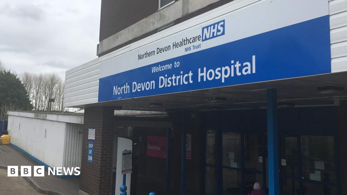 Outside one of the entrances to the North Devon District Hospital site. A blue and white sign with the hospital's name on it are above the main doors.