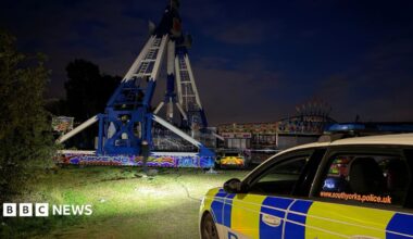 A police car parks in front of a fairground scene at night.
