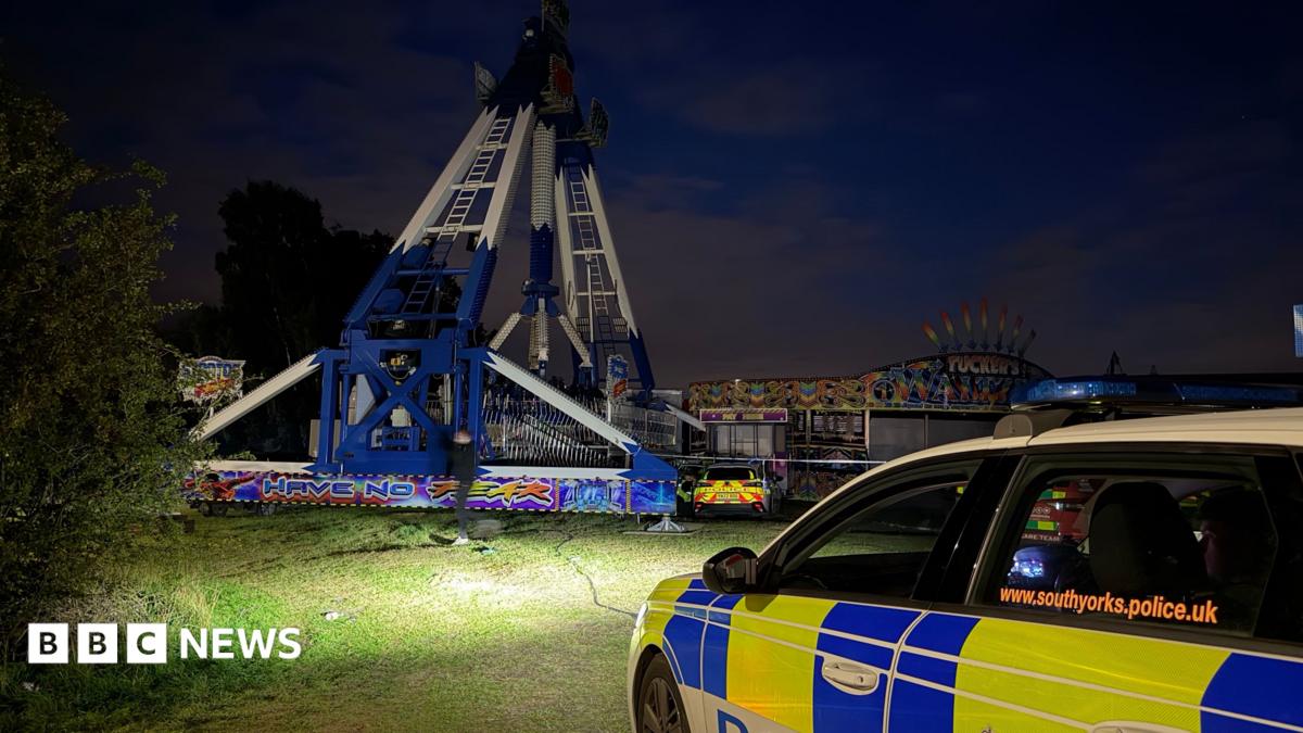 A police car parks in front of a fairground scene at night.