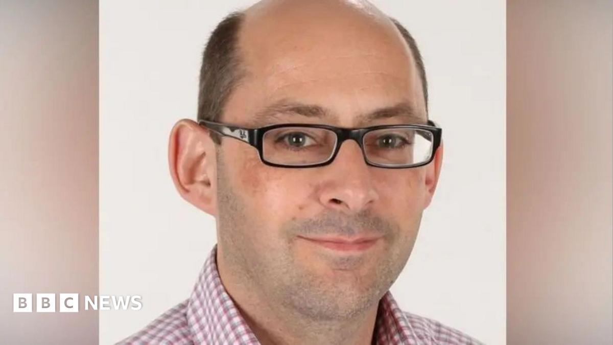 Mark, a man who wears glasses, he has a balding head and smiles.