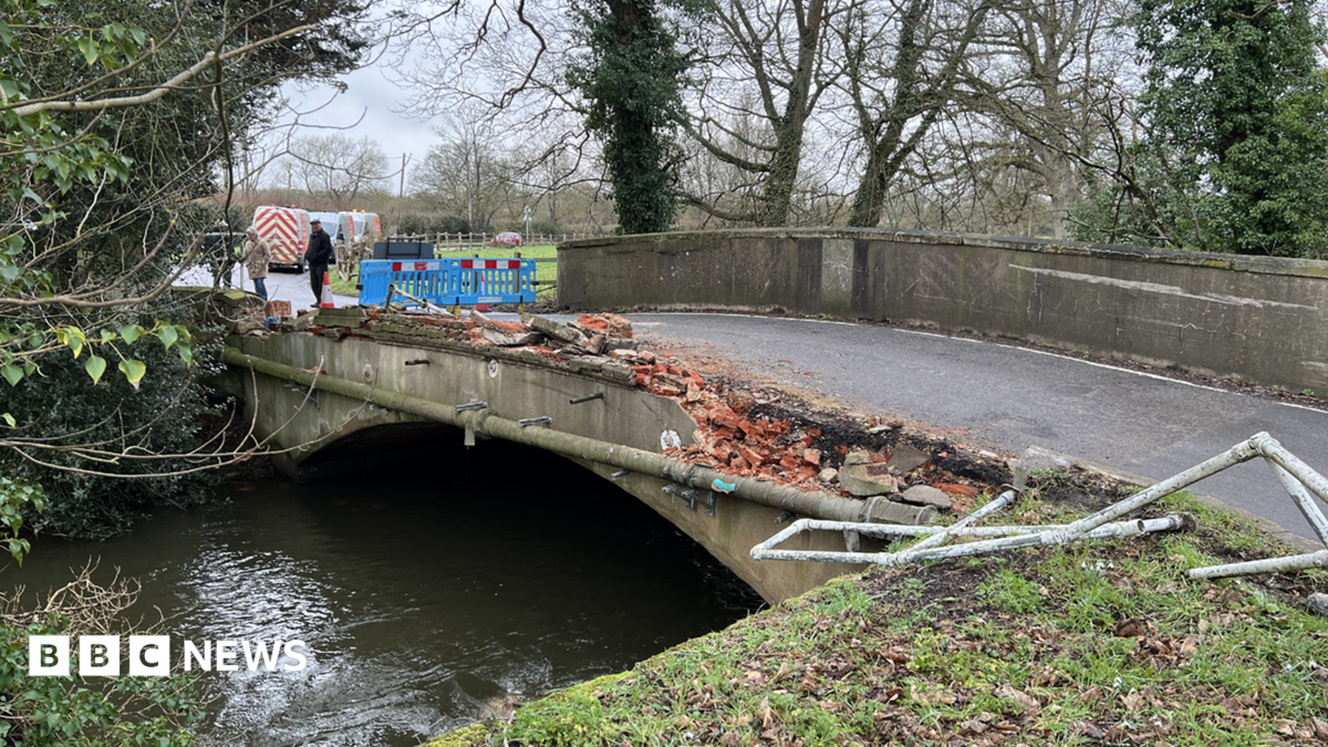 A general view picture of the bridge, which has seen its side closest to the camera totally flattened, with metal railings bent out of place and bricks scattered nearby.