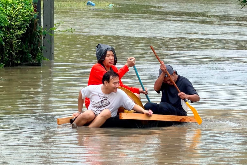 Three men in the middle of a flooded street, floating on top of a raft made of plywood.
