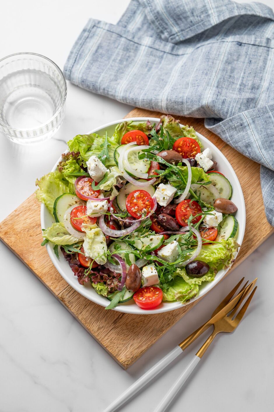 Fresh Greek salad with feta cheese, olives and vegetables in a plate on a marble table Fresh Greek salad with feta cheese, olives and vegetables in a plate on a marble table