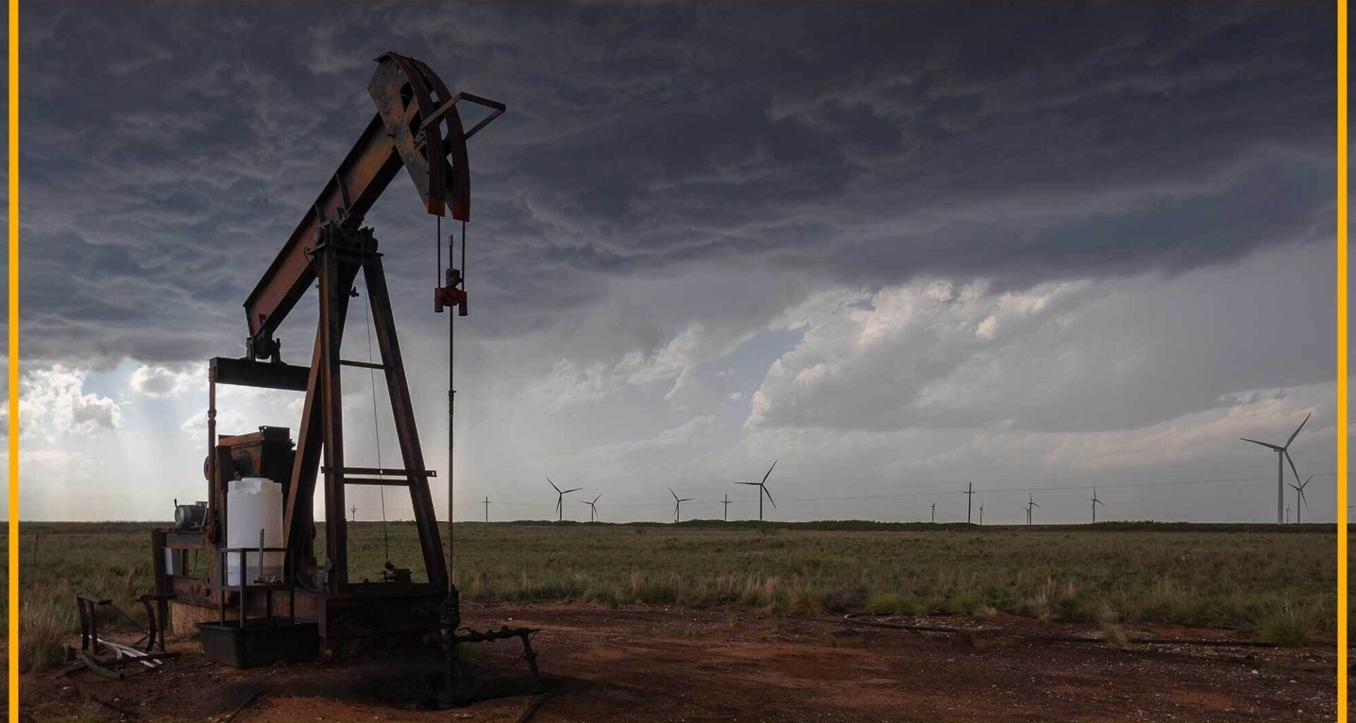 A close up of an oil rig with wind turbines in the background.