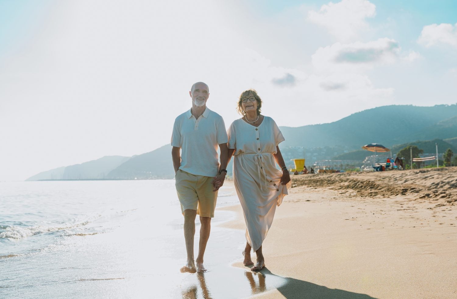 Happy senior couple enjoying their vacation, walking hand in hand along the ocean shoreline at sunset, reflecting love, companionship, and retirement joy