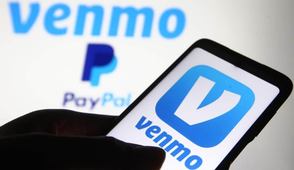 Venmo logo, a mobile payment service by Paypal, is displayed on a mobile phone screen and a monitor.