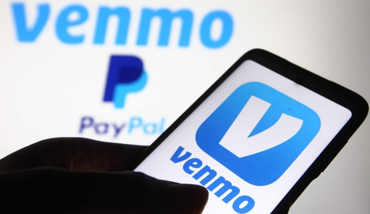 Venmo logo, a mobile payment service by Paypal, is displayed on a mobile phone screen and a monitor.