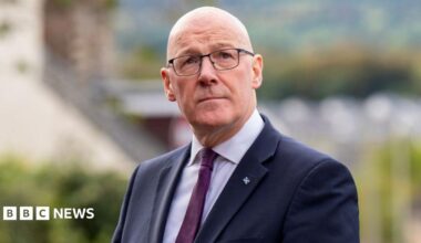 John Swinney, who is bald with glasses, gazing upwards. He is wearing a business suit