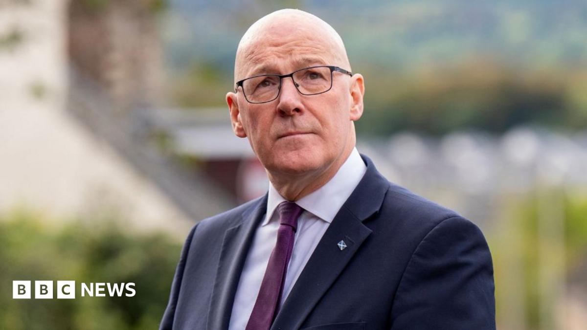 John Swinney, who is bald with glasses, gazing upwards. He is wearing a business suit