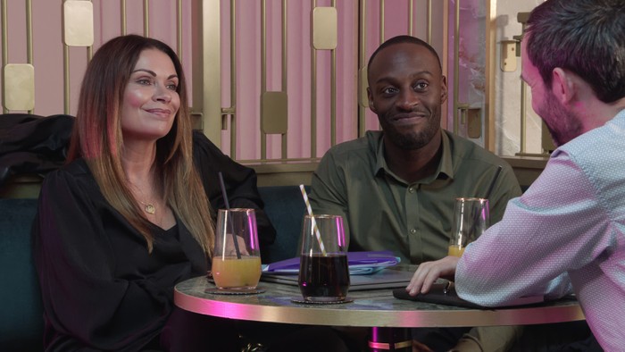 02_11_coro_carla_idris_02 Carla and Michael smile at a client in a scene from Coronation Street