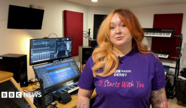 A woman stood in a recording studio wearing a purple BBC Radio Derby It Starts With You T shirt