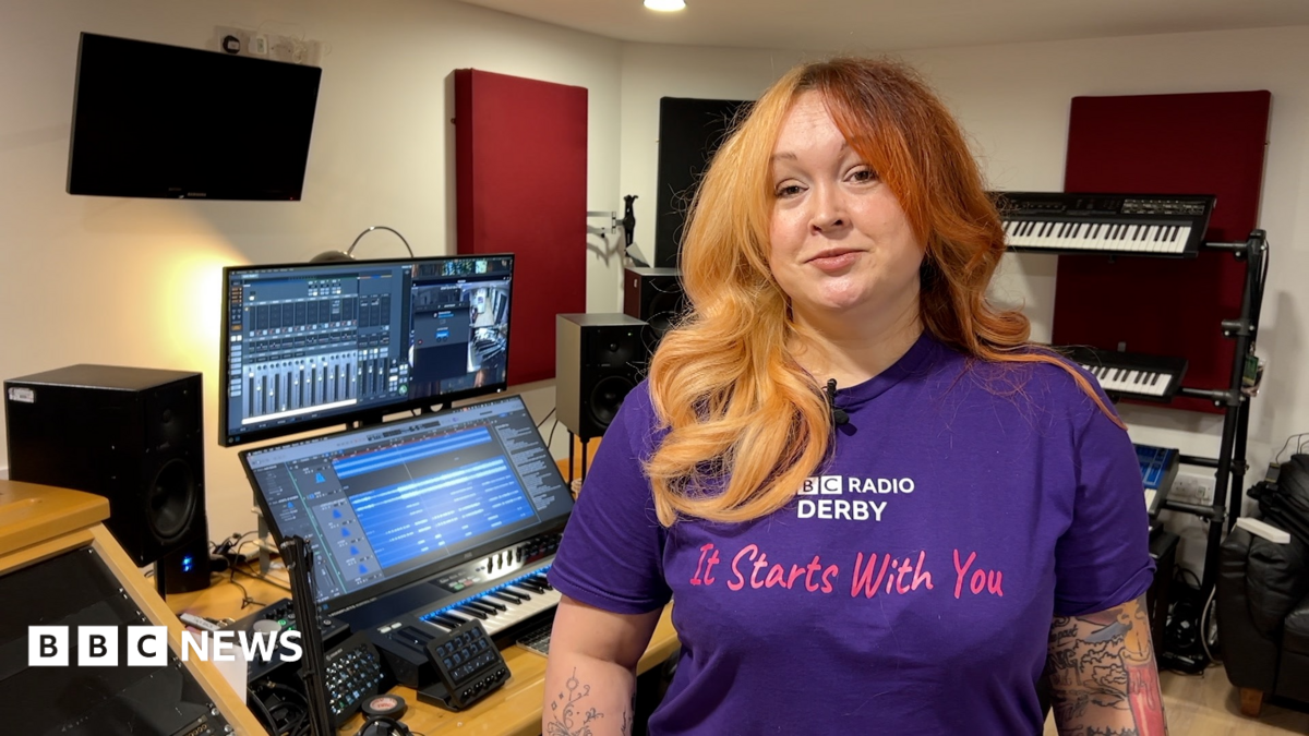 A woman stood in a recording studio wearing a purple BBC Radio Derby It Starts With You T shirt